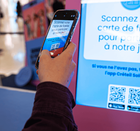 Scan carte de fidélité sur borne interactive pour participer à un jeu en magasin Client scannant sa carte de fidélité via smartphone sur une borne interactive pour accéder à un jeu promotionnel